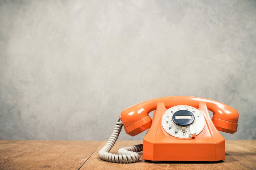 Sinnbild für Google Unternehmensprofil Hotline ist ein Retro-Telefon in Orange aus den 60er Jahren auf Holztisch