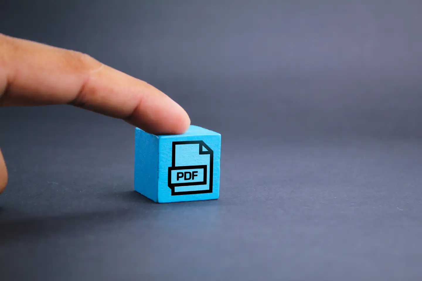 Finger zeigt auf einen blauen Würfel auf dem PDF steht