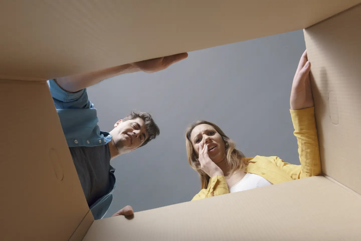 Paar öffnet Paket und Frau schaut entsetzt hinein, während sie die Hand an die Wange hält.